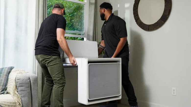Two people lifting a Gradient window heat pump into place in a window