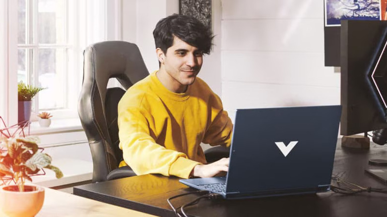 A person gaming on the HP Victus 15 laptop with a smile on their face, while sitting on a desk