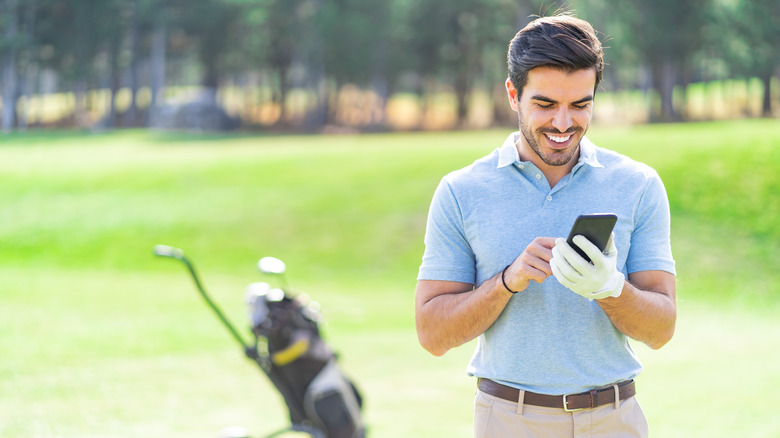 Jogador de golfe masculino usando smartphone no campo de golfe
