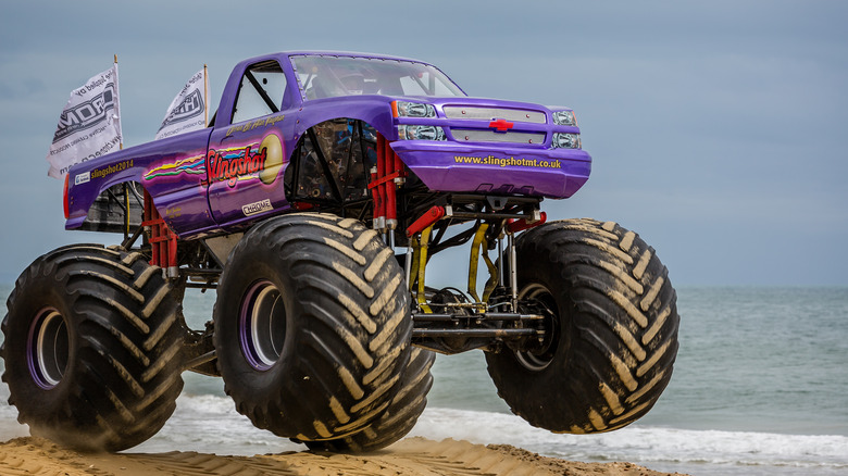 A purple monster truck at the beach, front 3/4 view