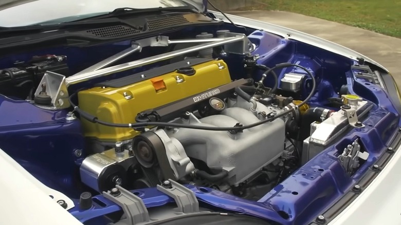 A heavily modified turbocharged K-24 four-cylinder engine with a bright yellow valve cover and custom strut bar sitting in a blue-painted engine bay.