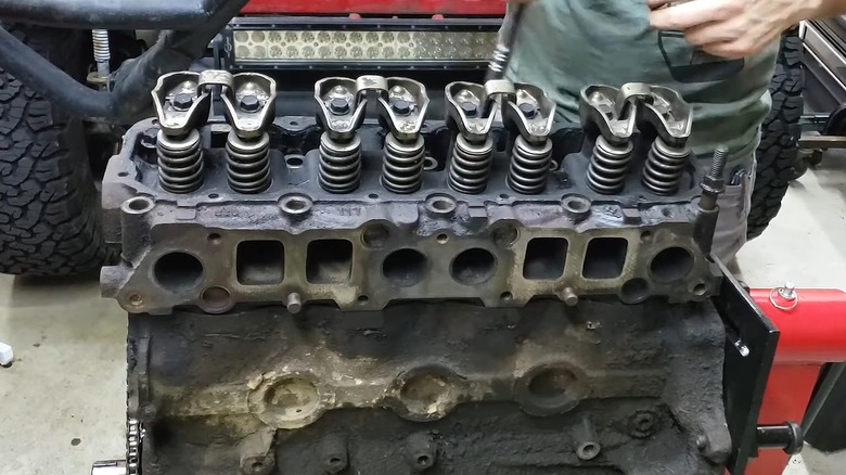 A wrench is on the valve springs of an exposed Jeep 2.5L's cylinder head