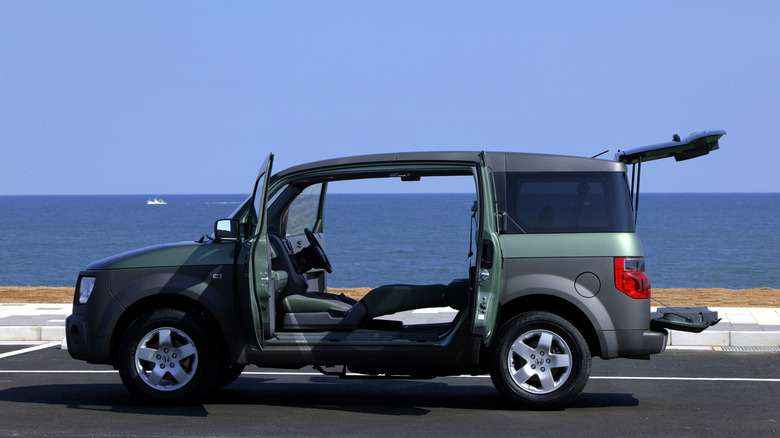 Green Honda Element SUV seen from left with clamshell doors open and ocean in background