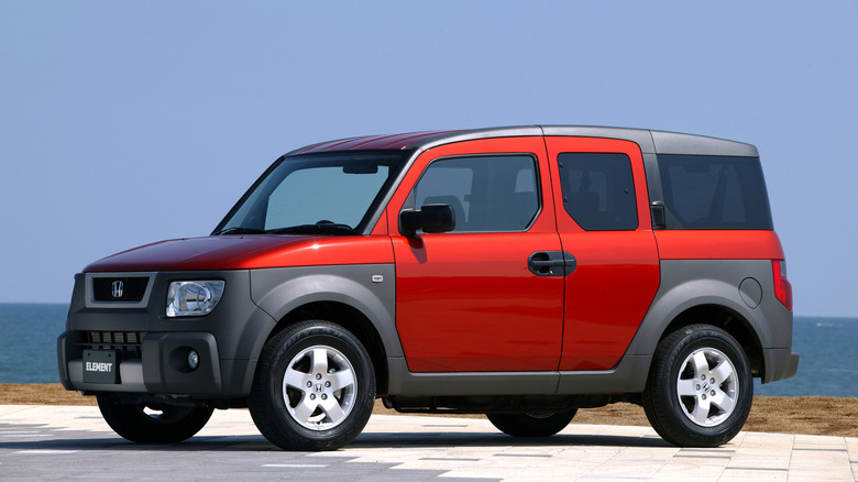 Red and gray Honda Element seen from the left in front of an ocean background
