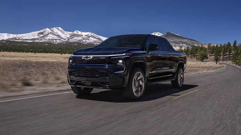 Black 2025 Silverado EV driving toward the camera on a two-lane road with snow-covered mountains in the background
