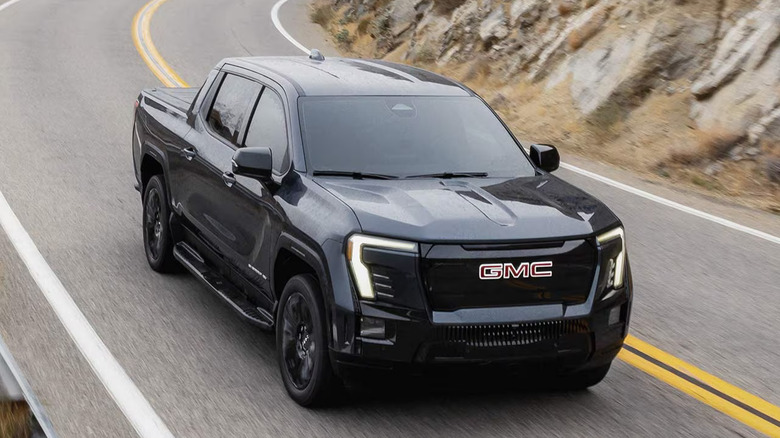 Black 2026 GMC Sierra EV driving toward the camera on a two-lane highway