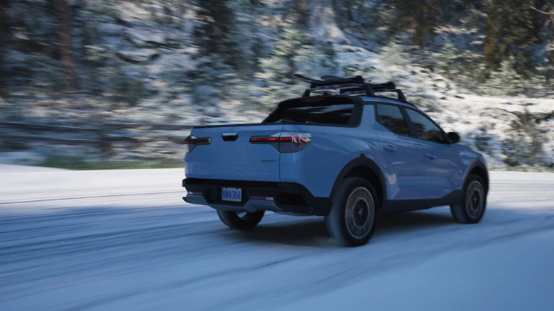 Blue Hyundai Santa Cruz driving away from the camera in a snowy landscape