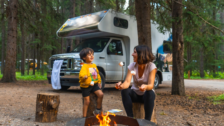 Woman and child roasting a marshmallow in front of a campfire with an RV in the background