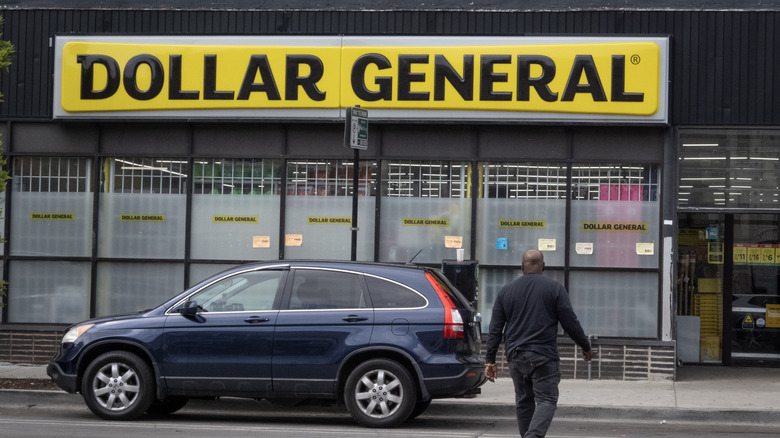 A car parked outside a Dollar General, and a person walking to the front door.