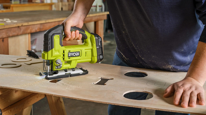 Craftsman holds down piece of lumber to cut through precise designs in lumber