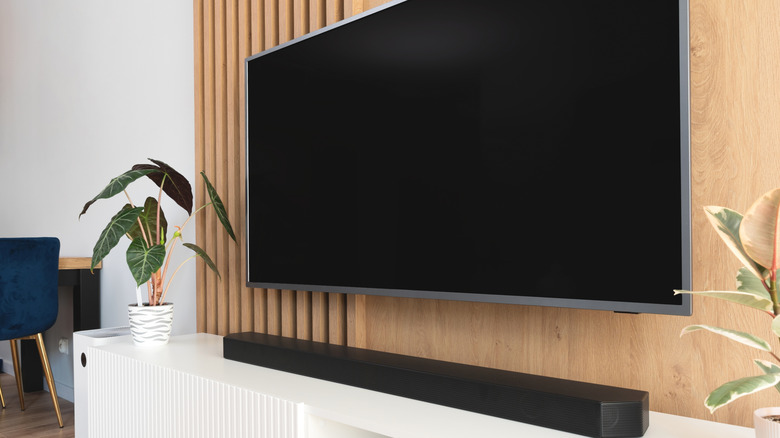 Black soundbar under a wall-mounted TV set against a wood paneled wall.