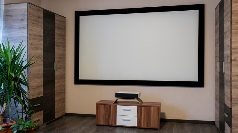 An ultra-short-throw projector sitting under a large screen in a home theater setup.