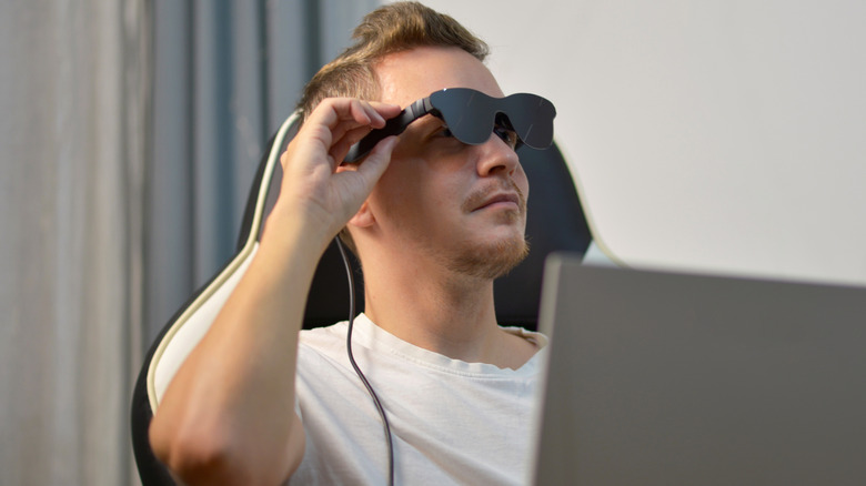 A person wearing smart XR glasses while sitting in a chair with a laptop.