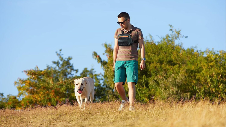 man with chest bag walking his dog