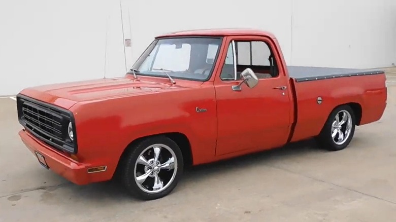 A solid red 1978 Dodge D100 sitting outside against a plain wall, looking like a resto-mod build with those polished five-spoke aftermarket wheels.
