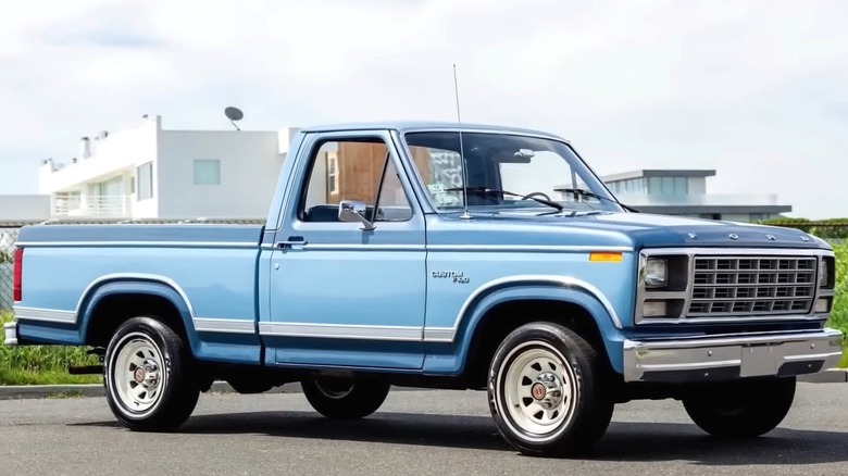 A clean light blue Ford F-150 Custom sits parked outdoors, looking surprisingly well-preserved for its age with those white steel wheels and that classic boxy early-'80s body.