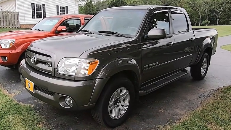 A dark gray Toyota Tundra Double Cab with the V8 badge on the fender sitting in a residential driveway next to a red Tacoma.