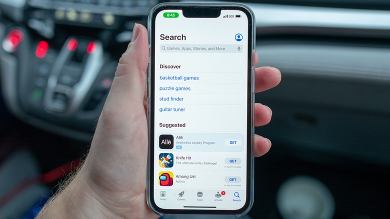 Person holding iPhone showing App Store search screen.