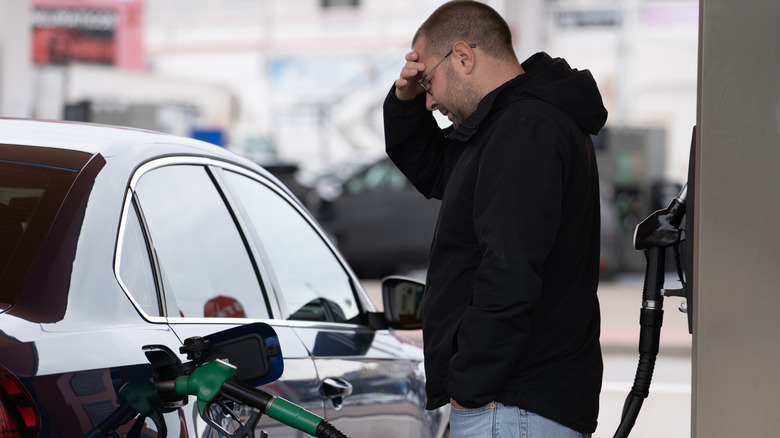 A frustrated-looking man filling up his black sedan with gas