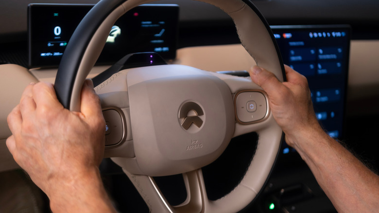 Hands on the steering wheel of a modern vehicle equipped with an airbag at the 9 and 3 o'clock positions.