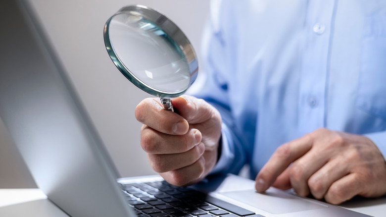 man using a magnifying glass to read on his laptop