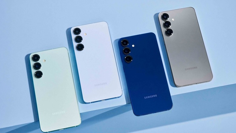 Four Samsung S25 units placed face-down on a light blue table, with two phones hanging off the edge a bit.