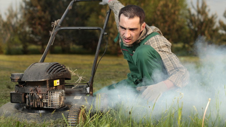 man looking at a smoking lawn mower