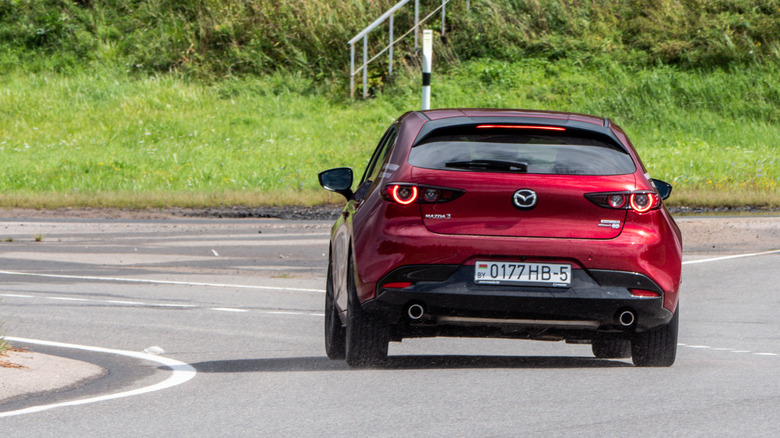 Rear view of a red Mazda3 on a roadway with foliage in the background