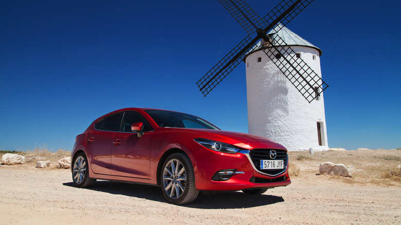 Red 2017 Mazda3 parked on dirt with a windmill in the background