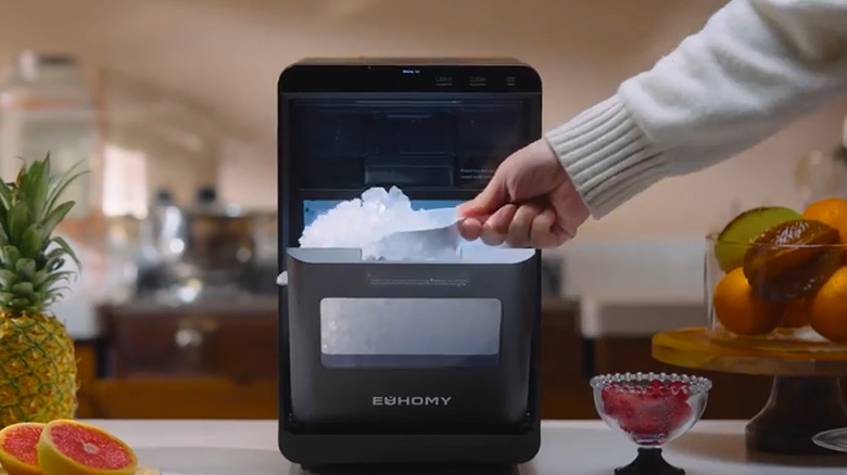 Person's hand scooping ice out of a countertop ice machine with a scoop