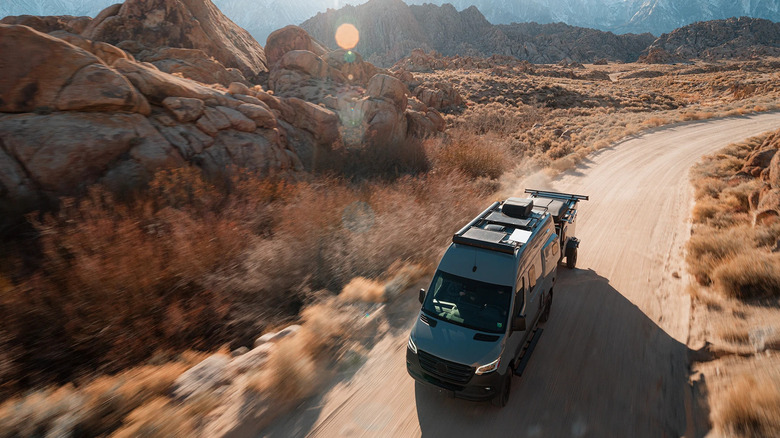Starlink Roam on top of a small RV traveling on a dirt road with rocks in the background