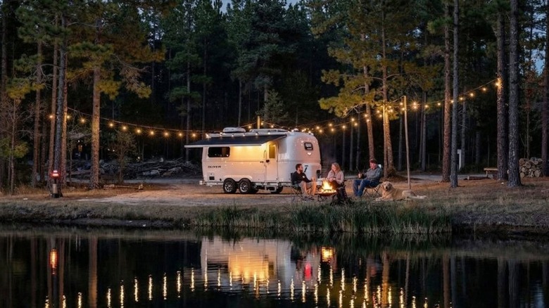 Oliver Legacy Elite II travel trailer parked near water at night with trees in the background and people in the foreground