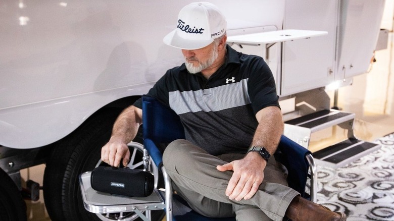 Person sitting in a camp chair next to an Oliver travel trailer with a Bluetooth speaker