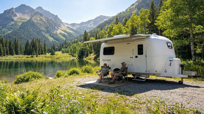 Two people sitting in camp chairs outside an Oliver travel trailer in an alpine setting
