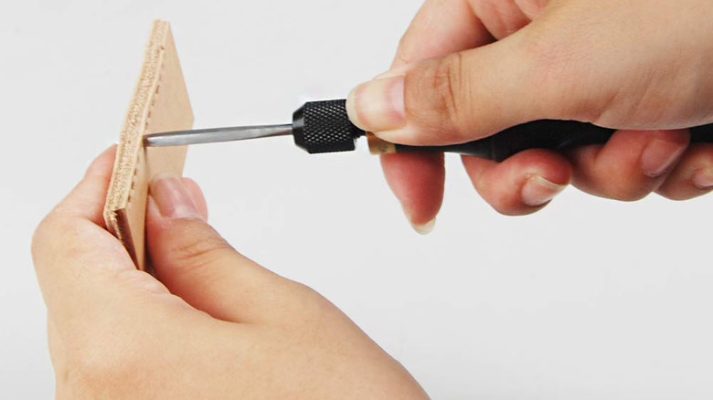 Awl being used to creature a stitching hole into a piece of leather