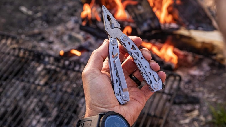 A multitool in the hand of someone near a fire.