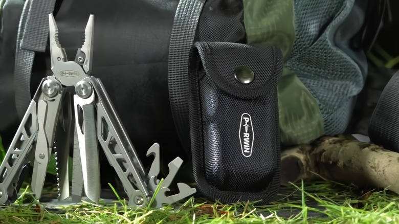 A multitool in the grass near a bag and carrying pocket.