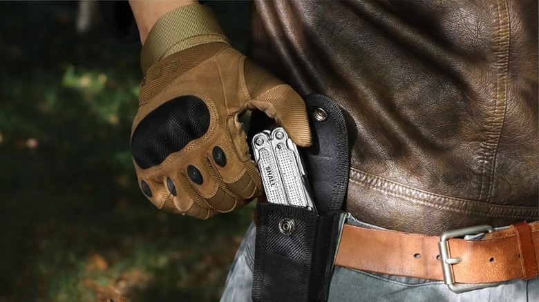 A multitool being put away into a pocket on a belt by someone in a forest.