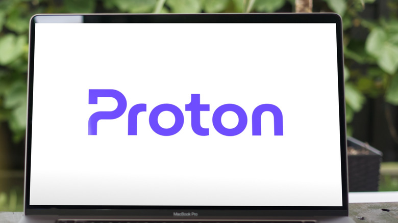 Proton logo on a laptop resting on a wooden table with shrubs in the background