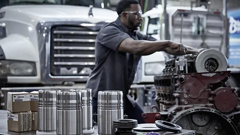 A person working on a Mack Truck engine in a garage