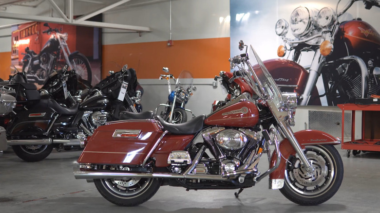 2006 Harley-Davidson Heritage Softail Classic Firefighter Edition FLSTC in Fire Engine Red with windshield, studded saddlebags, and chrome detailing, parked outside Pig Trail Harley-Davidson dealership
