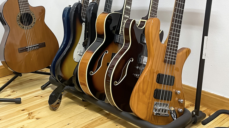 Many different bass guitars and guitars on a rack in a studio.