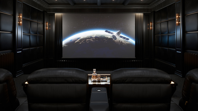 A luxurious home theater room with leather seats and an all-black aesthetic with a shot of a space shuttle on the screen
