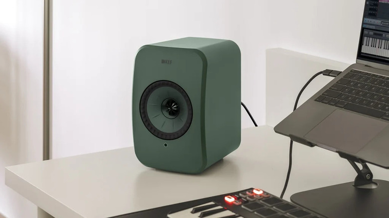 A green KEF LSX II LT bookshelf speaker on a white surface next to a laptop