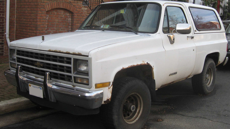 An older Chevrolet K5 Blazer parked by a brick apartment