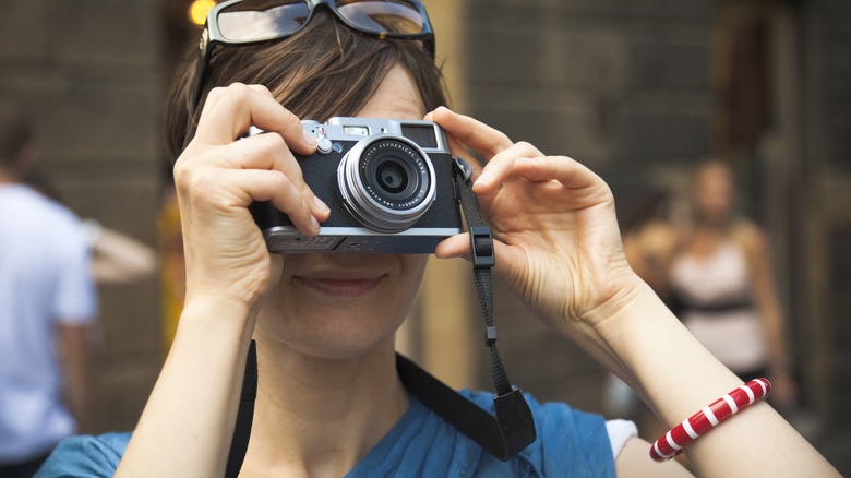 A woman taking photos with a Fujifilm X100 compact camera.