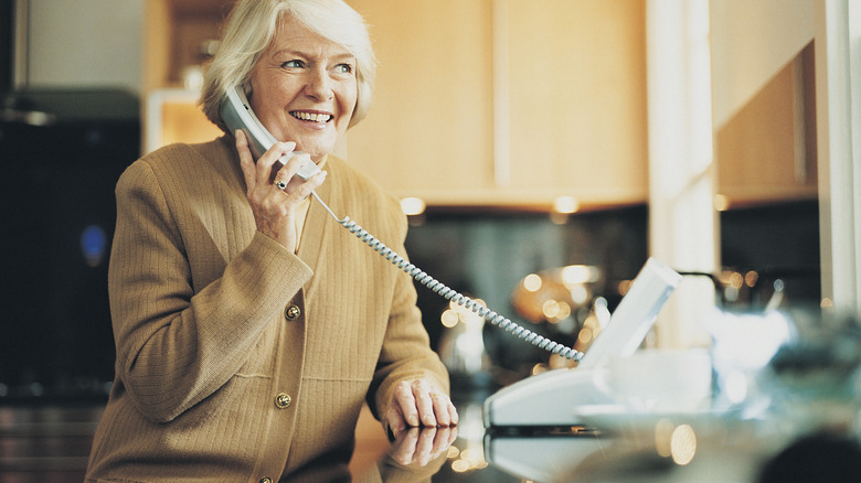 An elderly woman making a call on a landline phone.