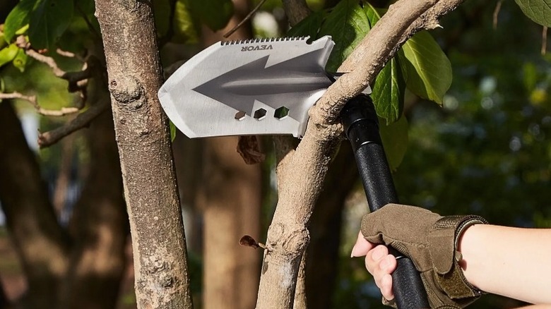 Gloved hand using the edge of a shovel to saw a small limb