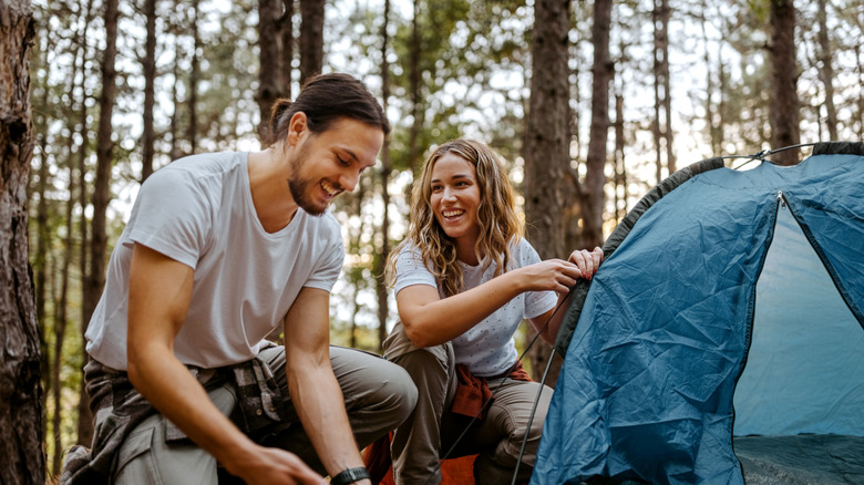 Two campers smiling while setting up their tent in the forest