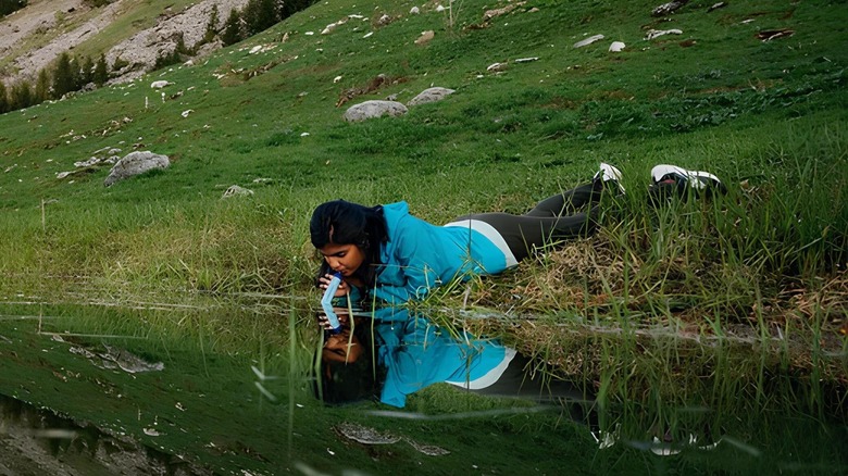 A woman drinking directly from a stream using a Lifestraw water filter